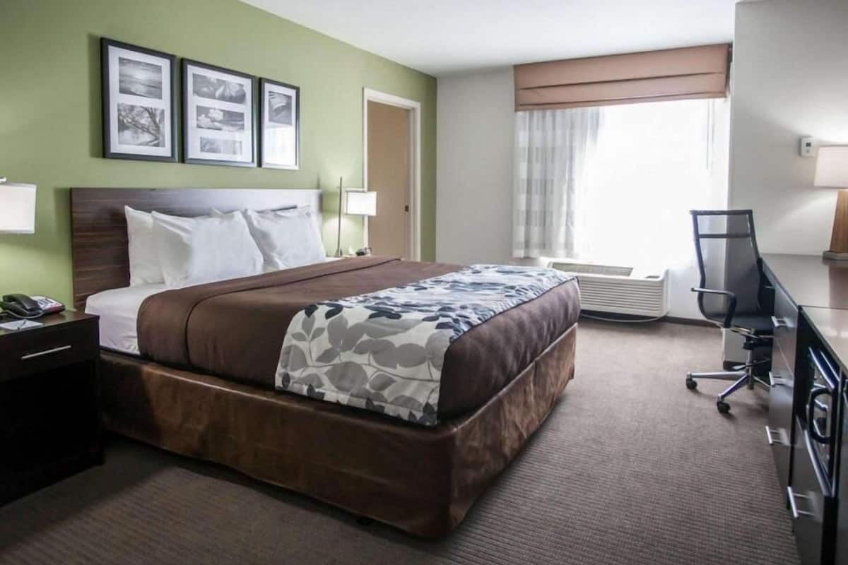 A hotel room with a large bed, a desk, a chair, and a window with curtains.