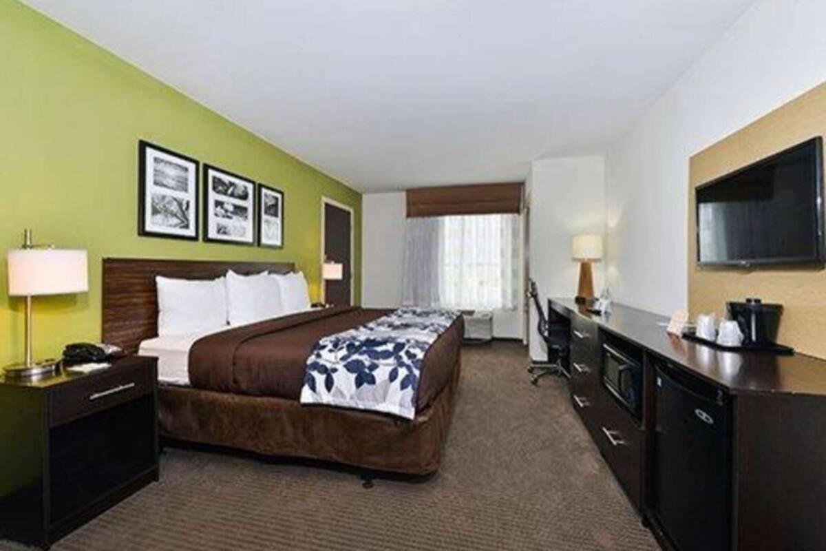 A hotel room with a bed, a desk, a TV, and a window with curtains.