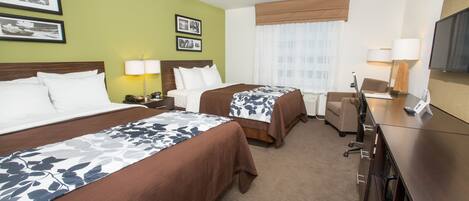 A hotel room with two beds, a desk, a chair, a TV, and a window with curtains.