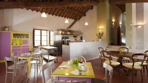 Un comedor con una mesa amarilla, sillas blancas y una cocina al fondo.