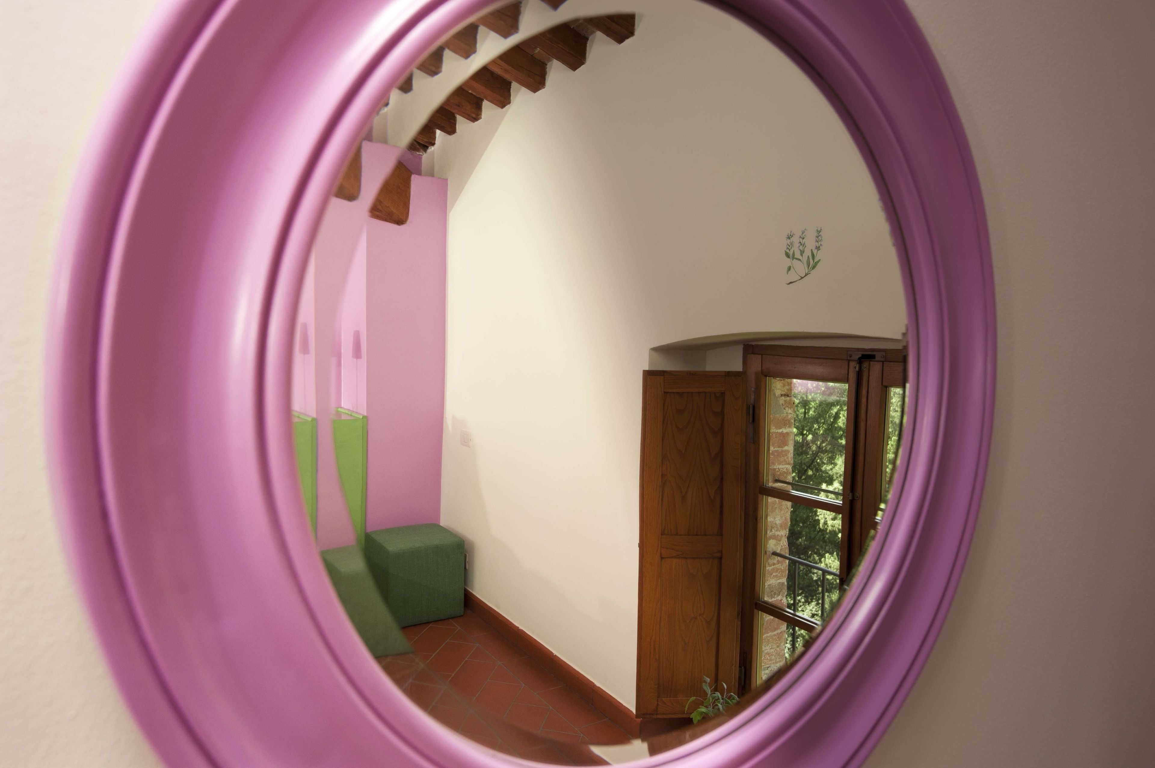 A room with a purple-framed mirror reflecting a staircase, a wooden door, and a green bench.