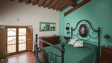 A bedroom with a wooden bed frame, a green bedspread, a wooden dresser, a mirror, and a window with a view of a balcony.