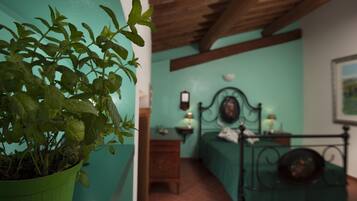 A room with a bed, bedside table, lamp, and a potted plant.