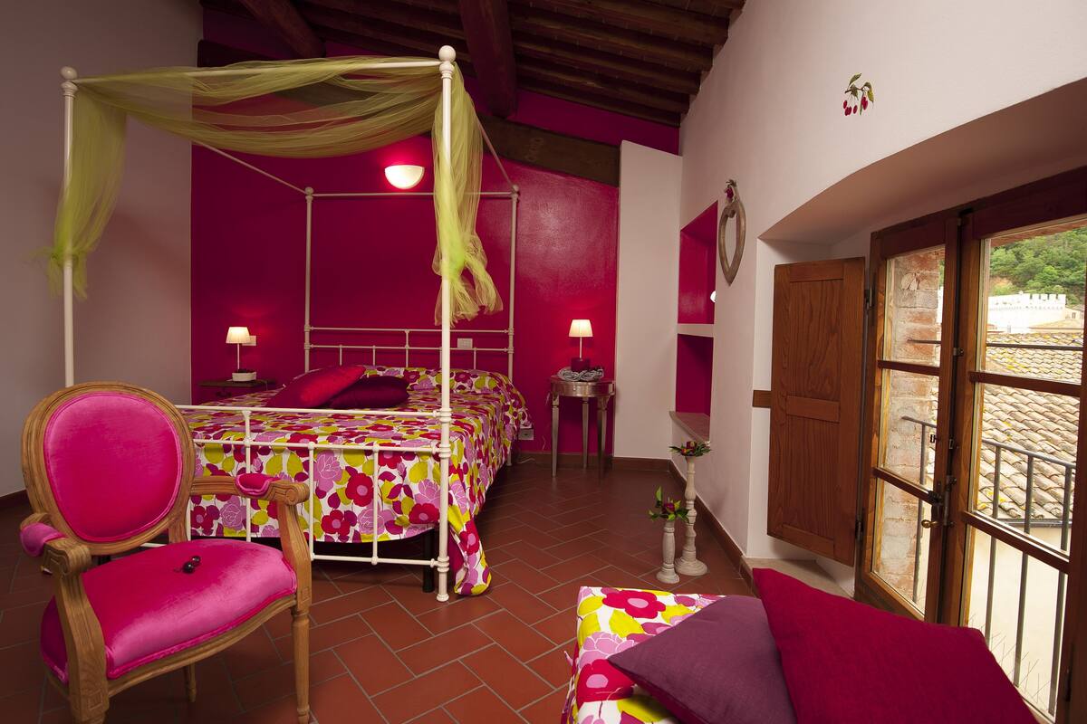 A bedroom with a four-poster bed, a chair, and a window with a view of a building.