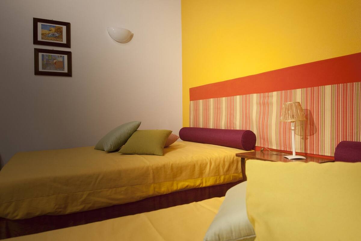A hotel room with two beds, a nightstand, a lamp, and a striped wall.