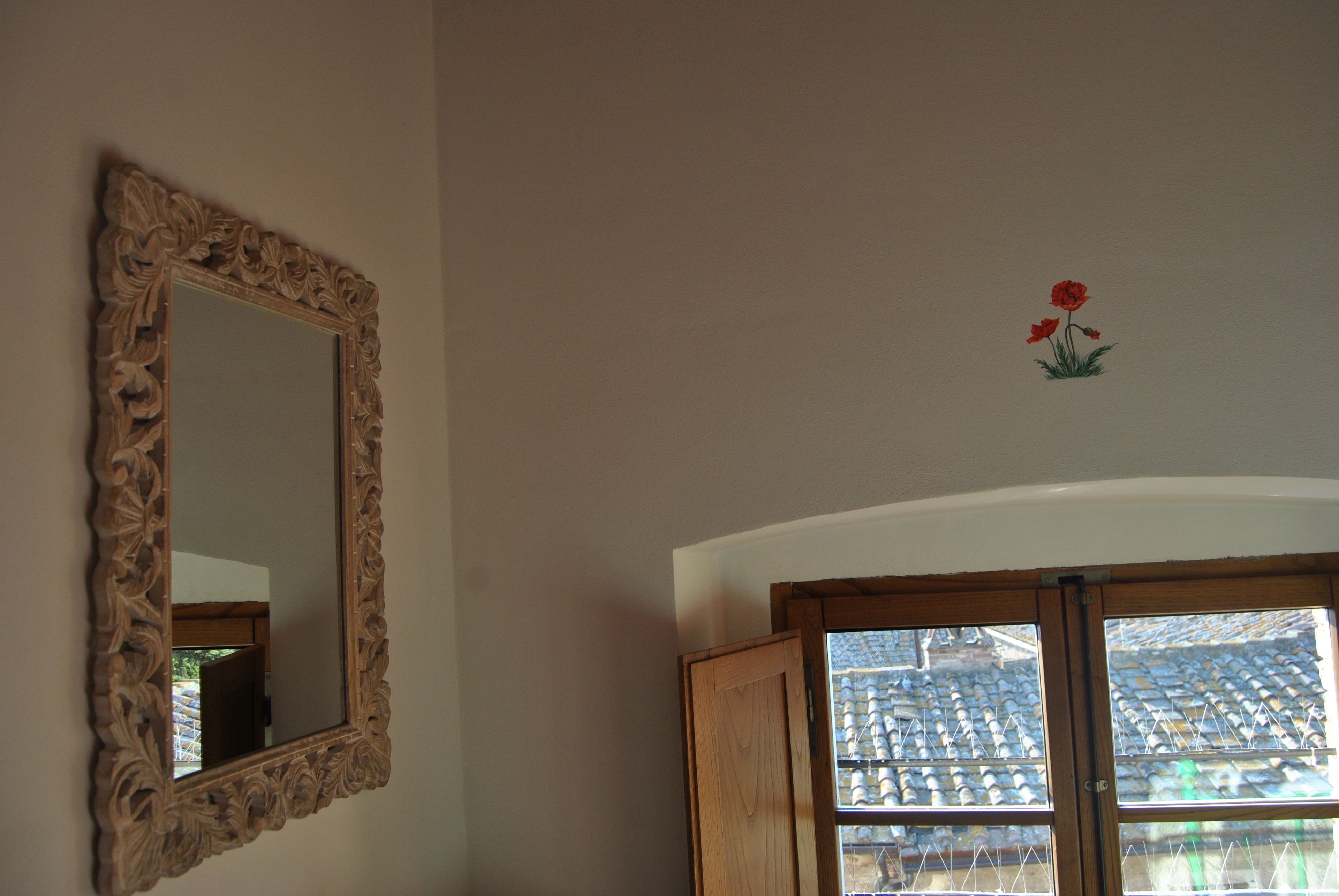 A room with a large ornate mirror, a wooden door, and a small flower decoration on the wall.