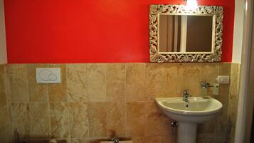 Ein Badezimmer mit roter Wand, Marmorboden, einem Standwaschbecken, einem an der Wand befestigten Spiegel und einer Toilette.