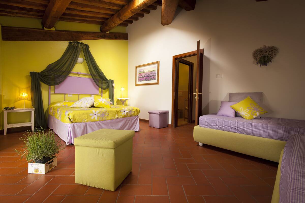 A bedroom with two beds, a small table, a nightstand, a potted plant, and a door leading to another room.