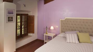 A bedroom with a skylight, a bed with striped bedding, a nightstand with a lamp, and a window with shutters.