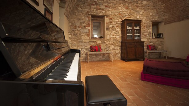 Una habitación con un piano, paredes de piedra, un mueble de madera y un banco.