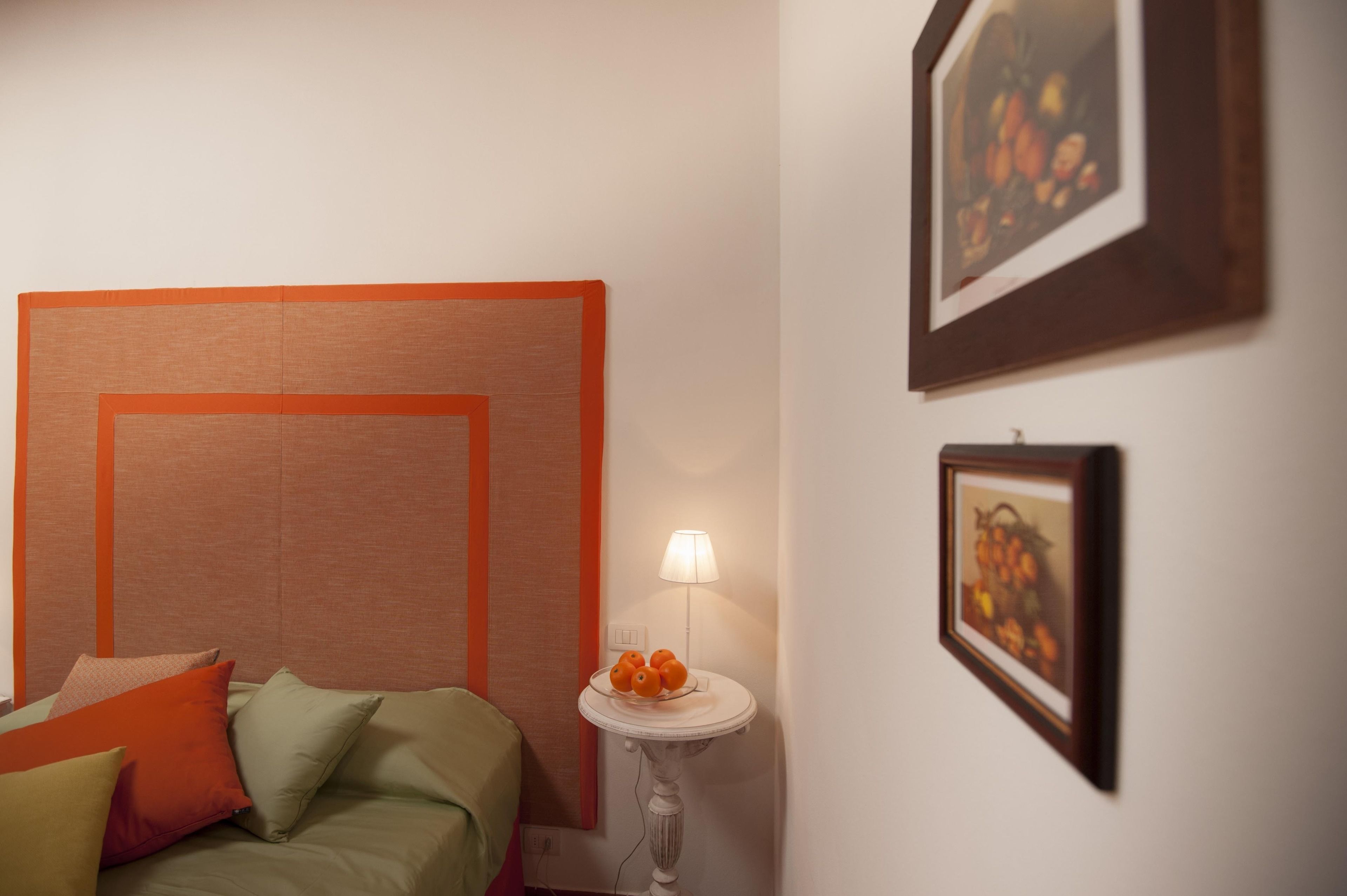 Une chambre à coucher avec un lit, des oreillers, une table de chevet avec une lampe et des œuvres d’art encadrées accrochées au mur.