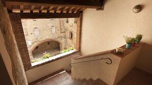 Una escalera estrecha con un pequeño ventanal que da a un patio con un edificio de ladrillo y un techo de madera.