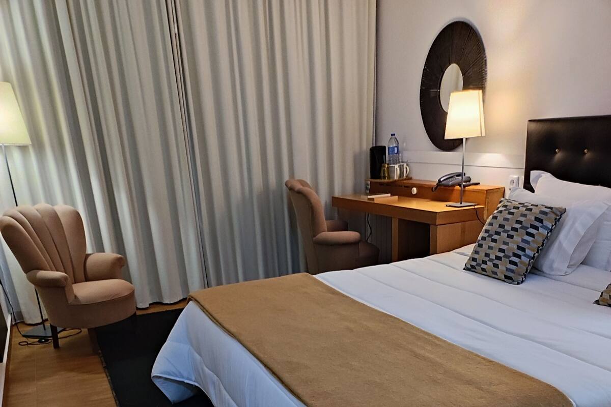 Hotellihuone, jossa on suuri sänky, työpöytä, tuoli ja lamppu.