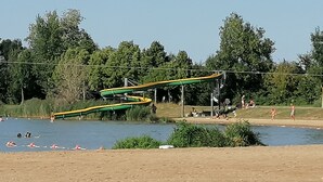 Parque acuático con río lento, toboganes verdes y amarillos, y una zona de playa con arena.