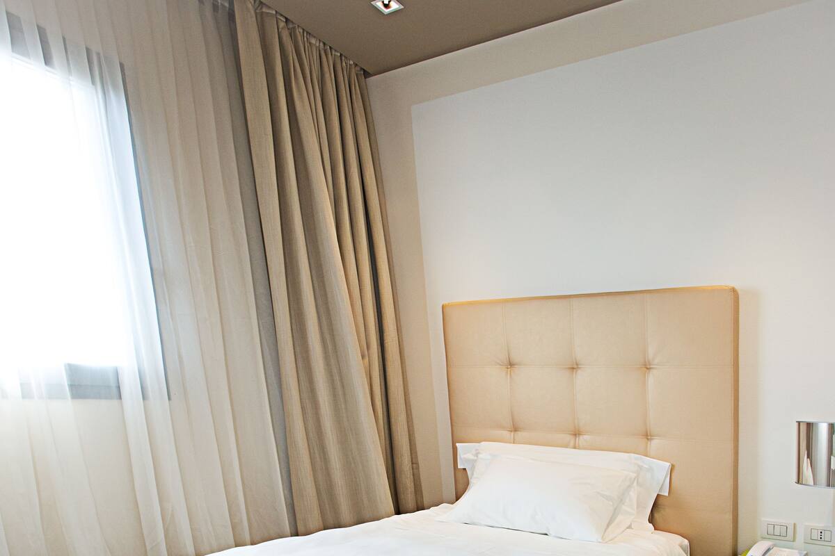 Quarto de hotel com uma cama grande, uma mesa de cabeceira verde e um tapete estampado com padrão de zebra.