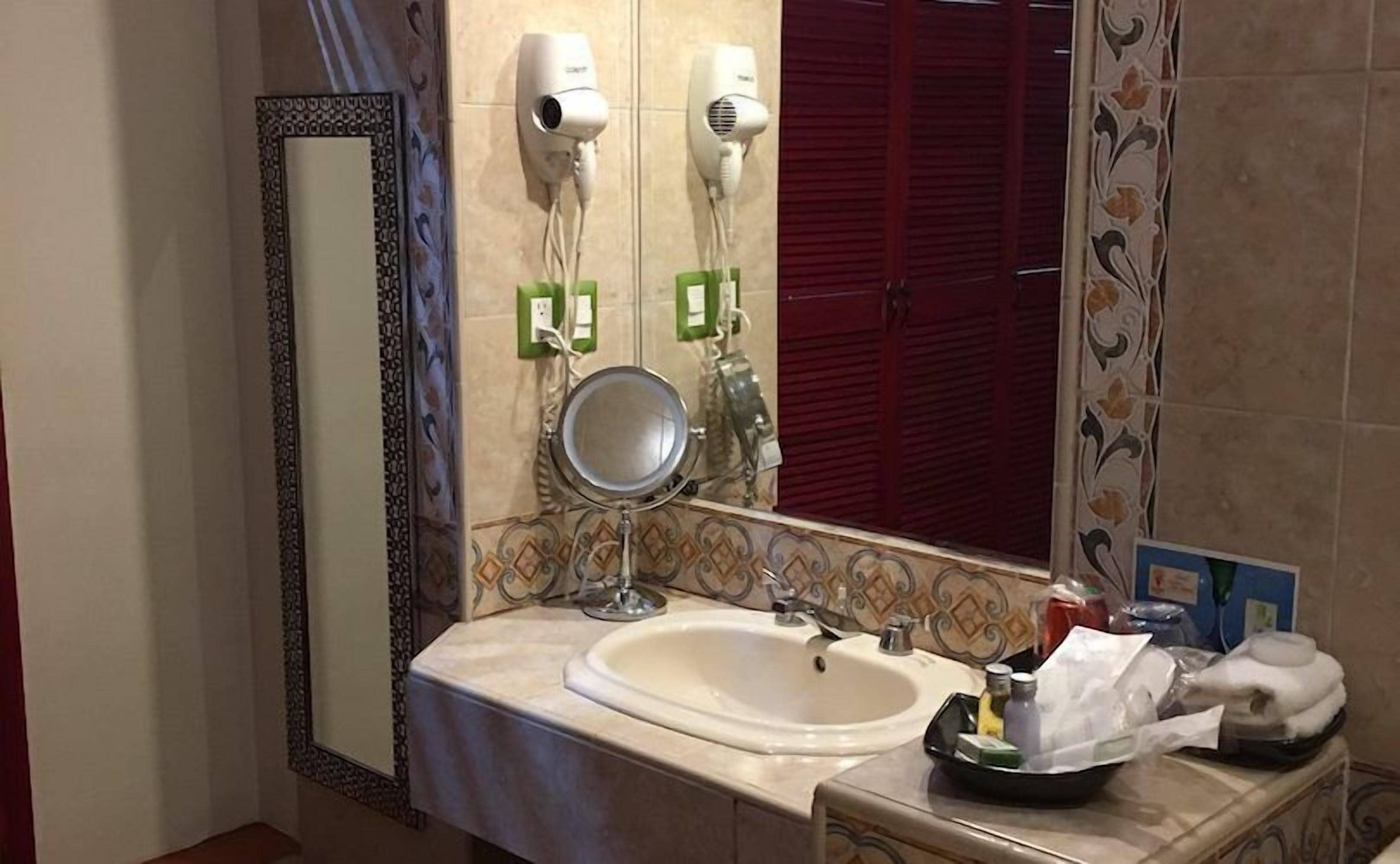 Un baño con lavamanos, espejo, secador de pelo y toallero.