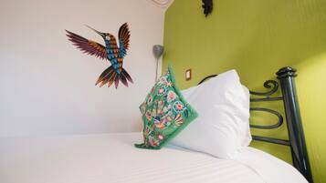 Un letto con biancheria bianca, un cuscino verde con motivi floreali e una decorazione a forma di uccello appesa al muro.