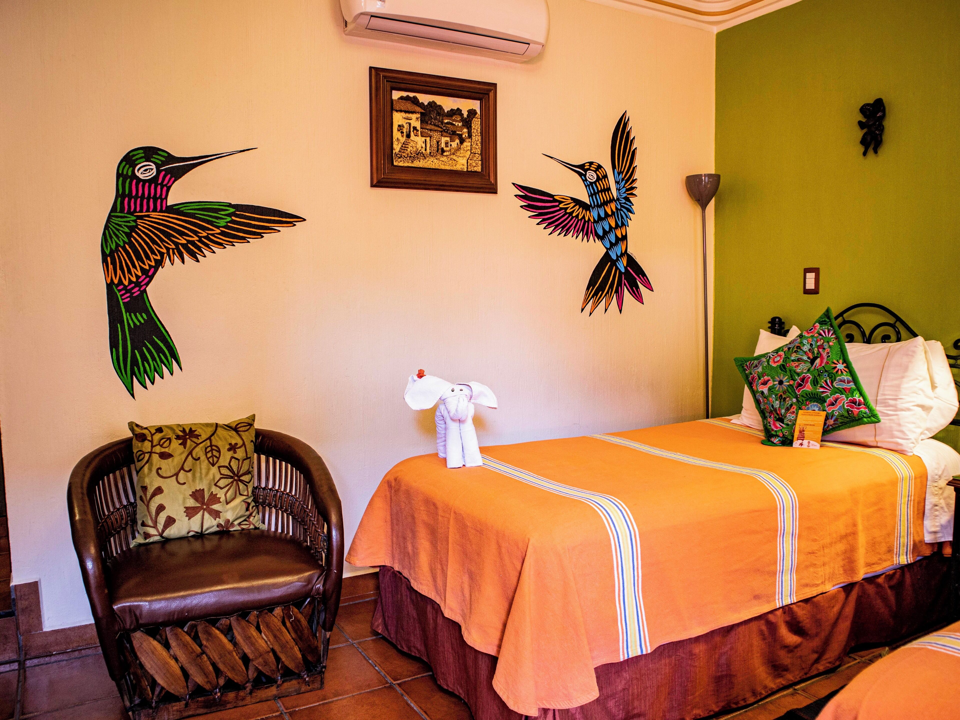 A hotel room with a bed, a chair, and two wall-mounted wall art pieces.