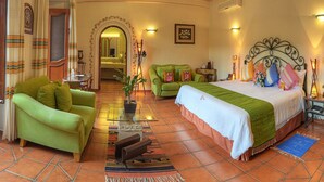 Une chambre d’hôtel avec un canapé vert, un lit recouvert d’une couverture verte, une petite table avec une lampe, et une salle de bain visible à travers une arche.