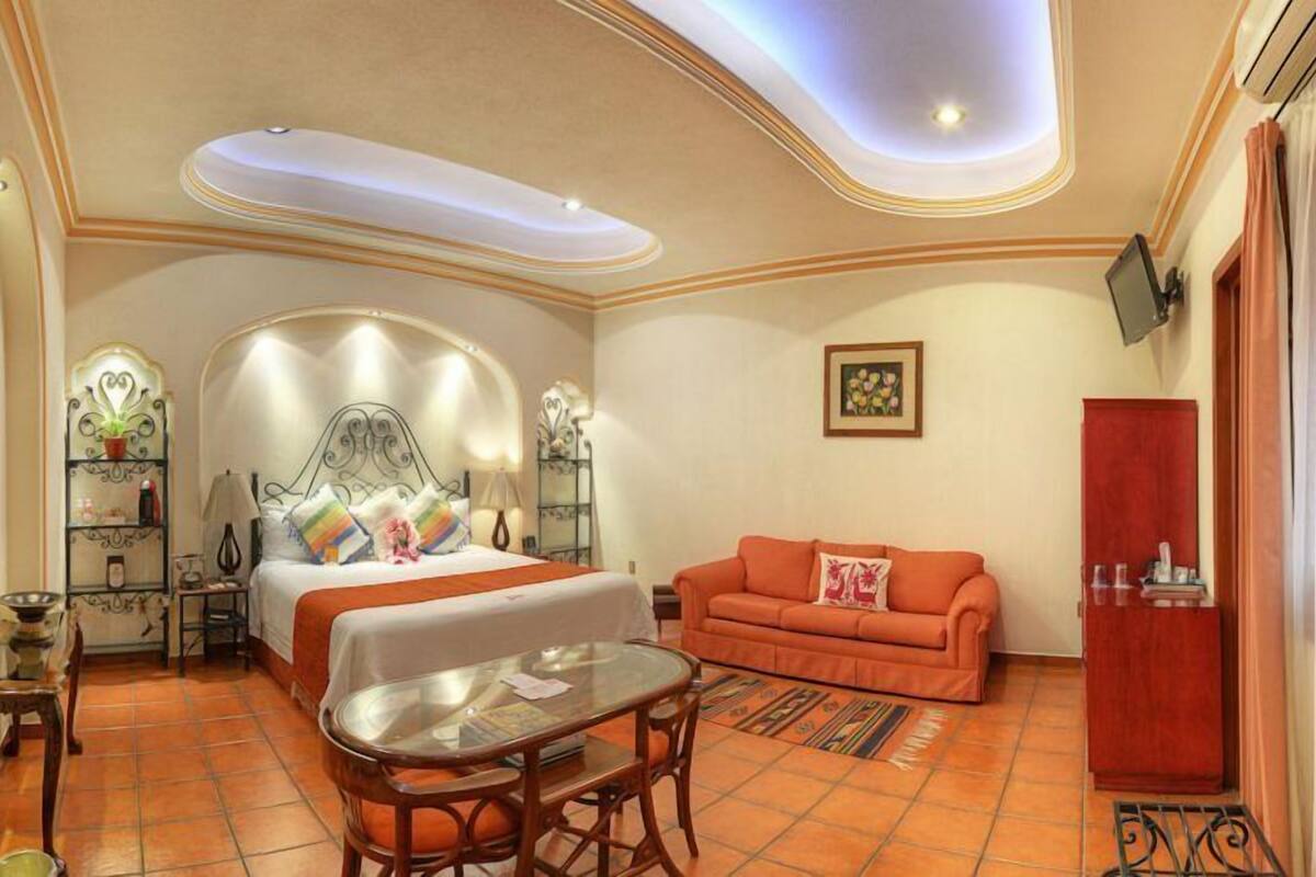 A hotel room with a bed, a sofa, a small table, and a TV.