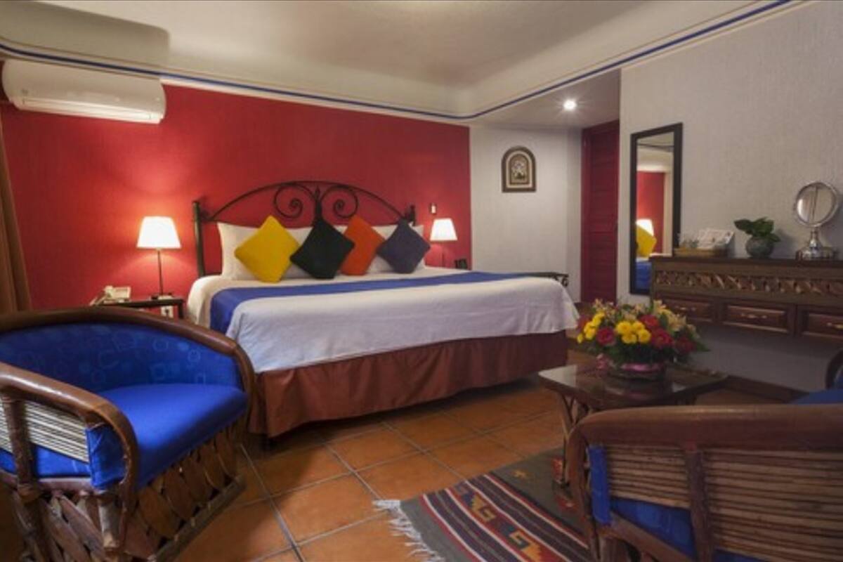 A hotel room with a bed, two chairs, a dresser, and a mirror.