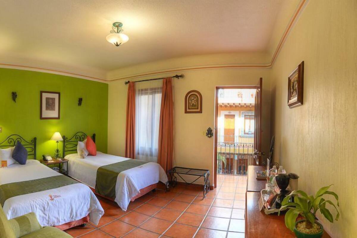 A room with two beds, a green wall, a tiled floor, and a balcony with a view.