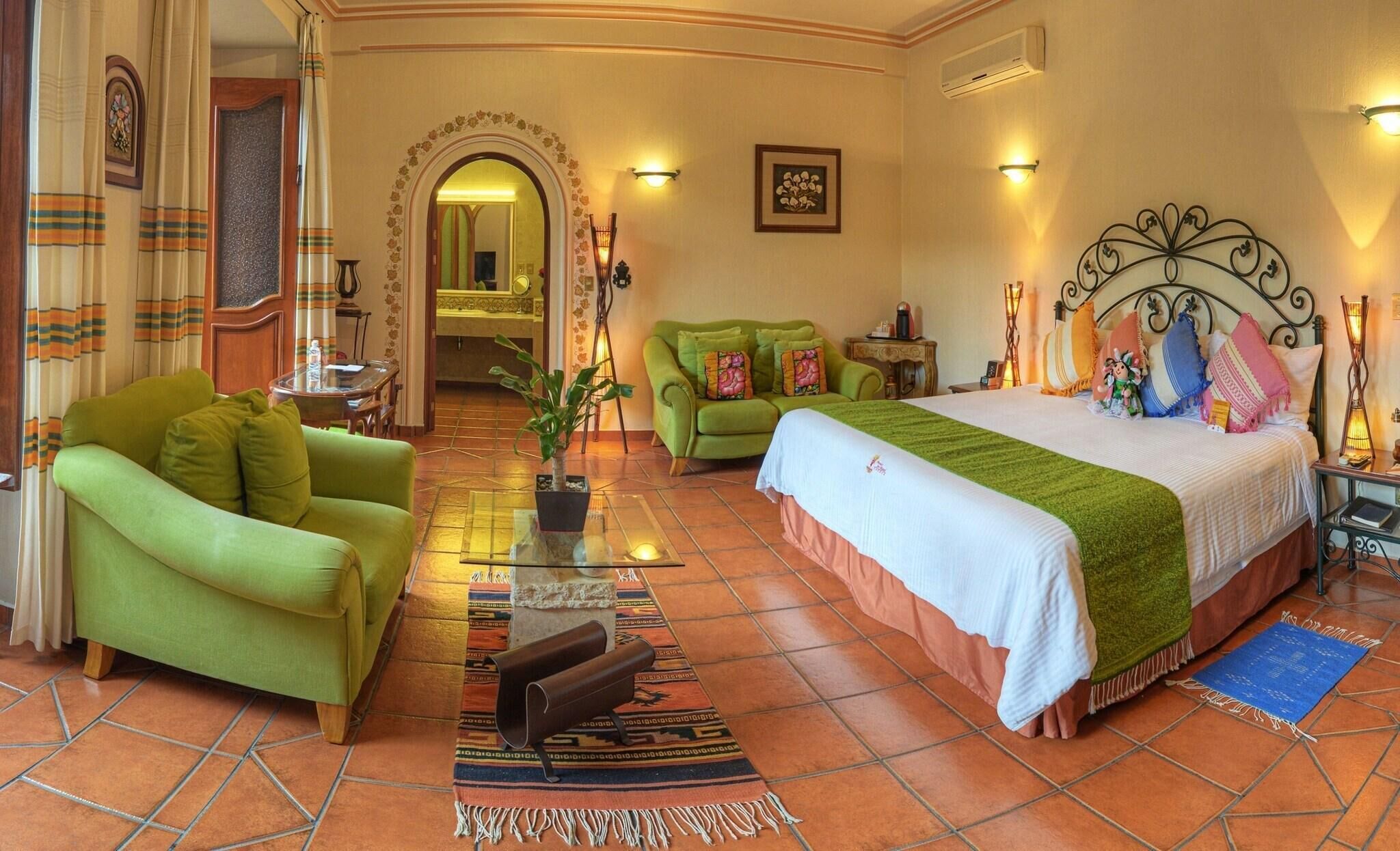A hotel room with a bed, a sofa, a coffee table, and a dining area.