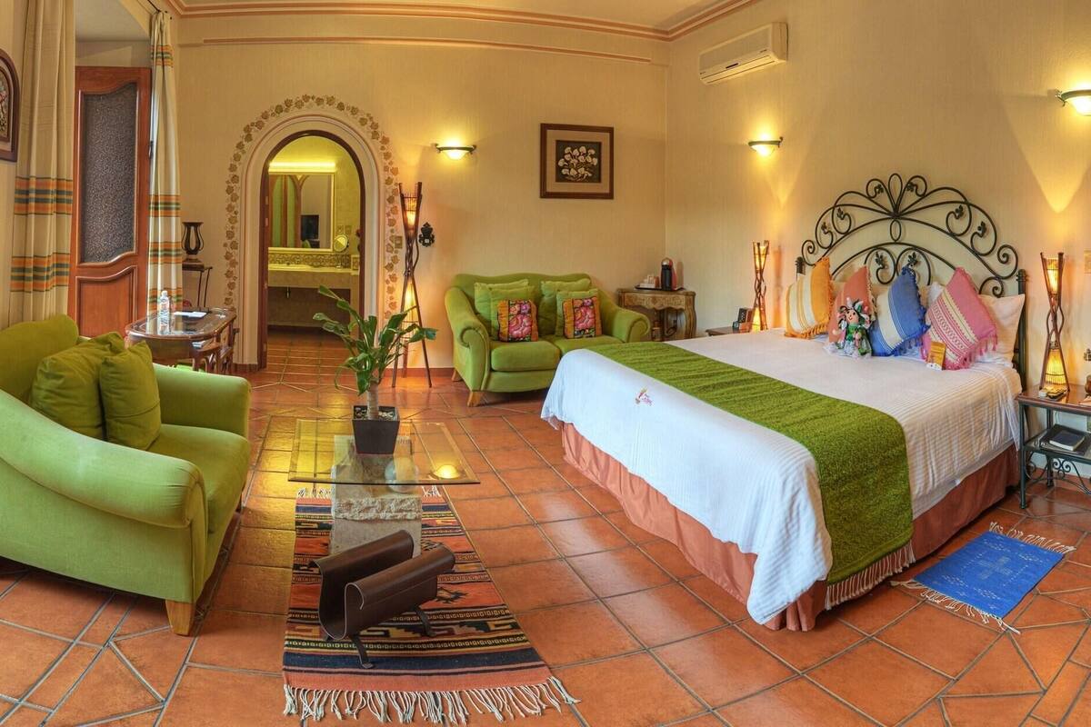 A hotel room with a bed, a sofa, a coffee table, and a dining area.