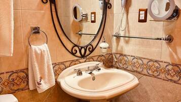 Un baño con lavamanos pedestal, un perchero con toalla blanca, un secador de pelo y un espejo con marco decorativo.