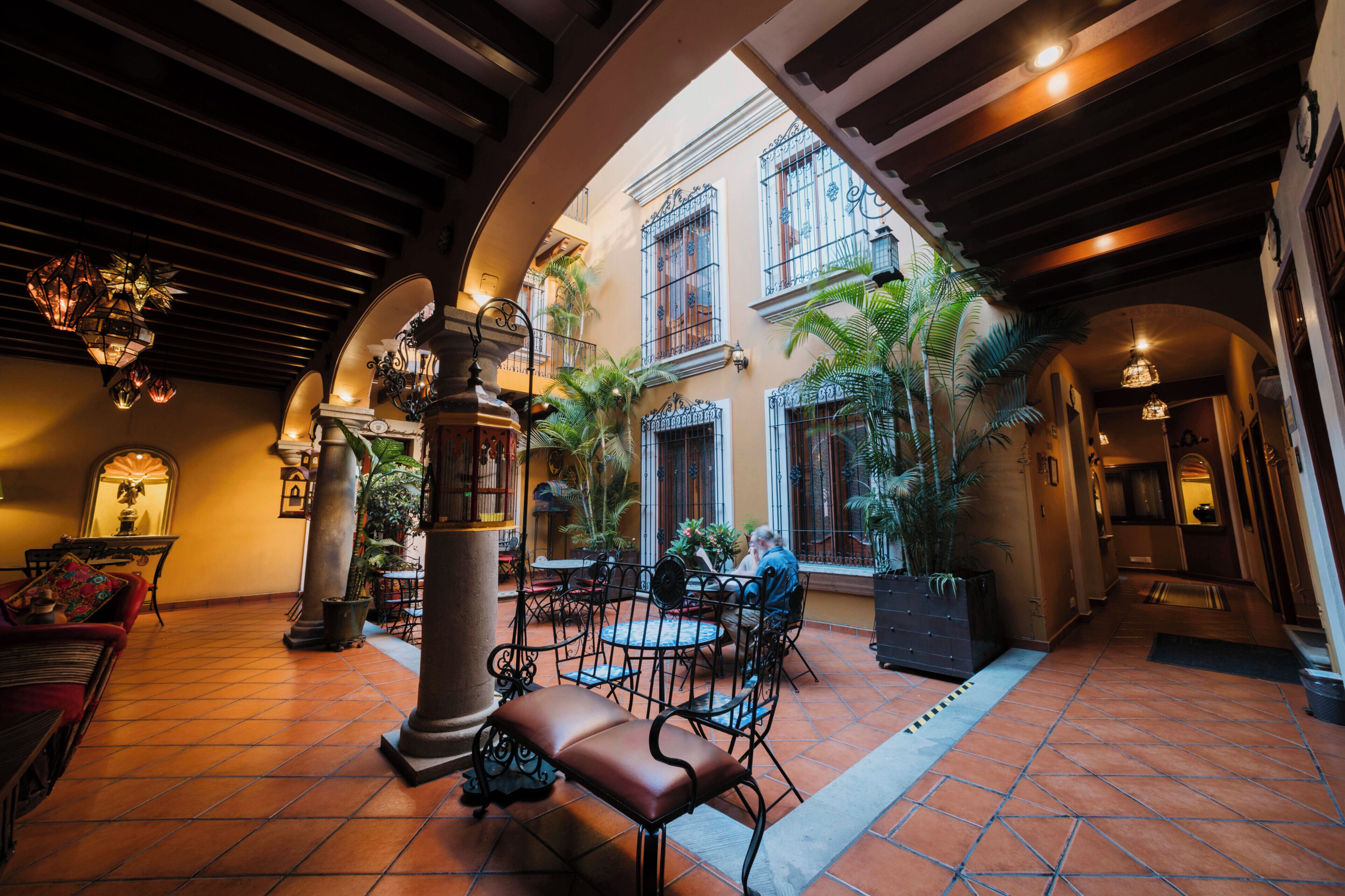 An indoor courtyard with a tiled floor, a central seating area with chairs and a table, and a large pillar.