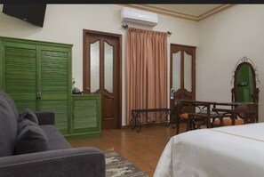 A room with a green wardrobe, a bed, a table with chairs, and a mirror.