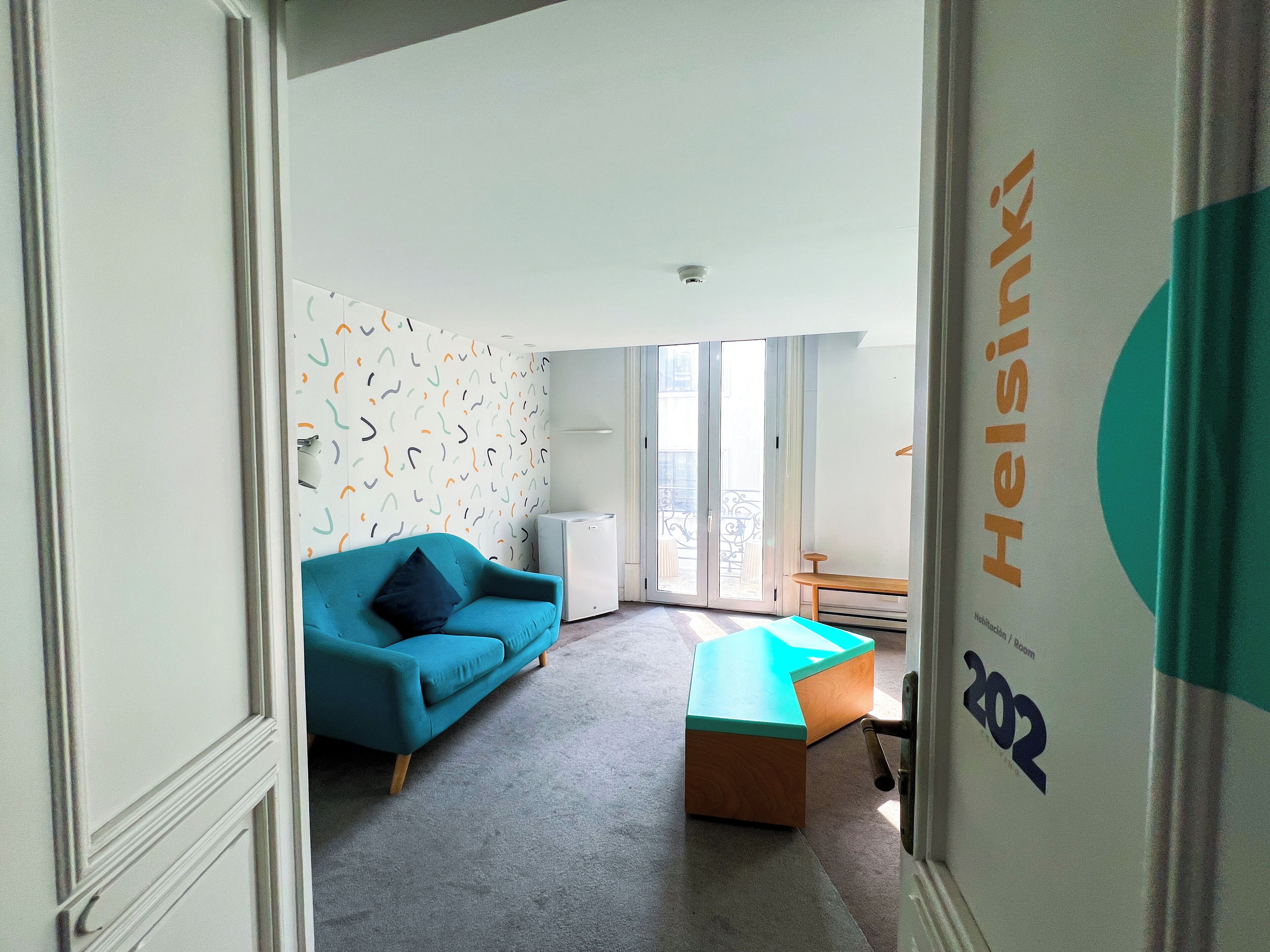 Una habitación moderna con un sofá azul, un banco de madera y una pared con diseño.