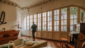 A spacious room with large windows, a piano, wicker furniture, and a cozy seating area. - Viajero Montevideo Hostel (Montevideo)