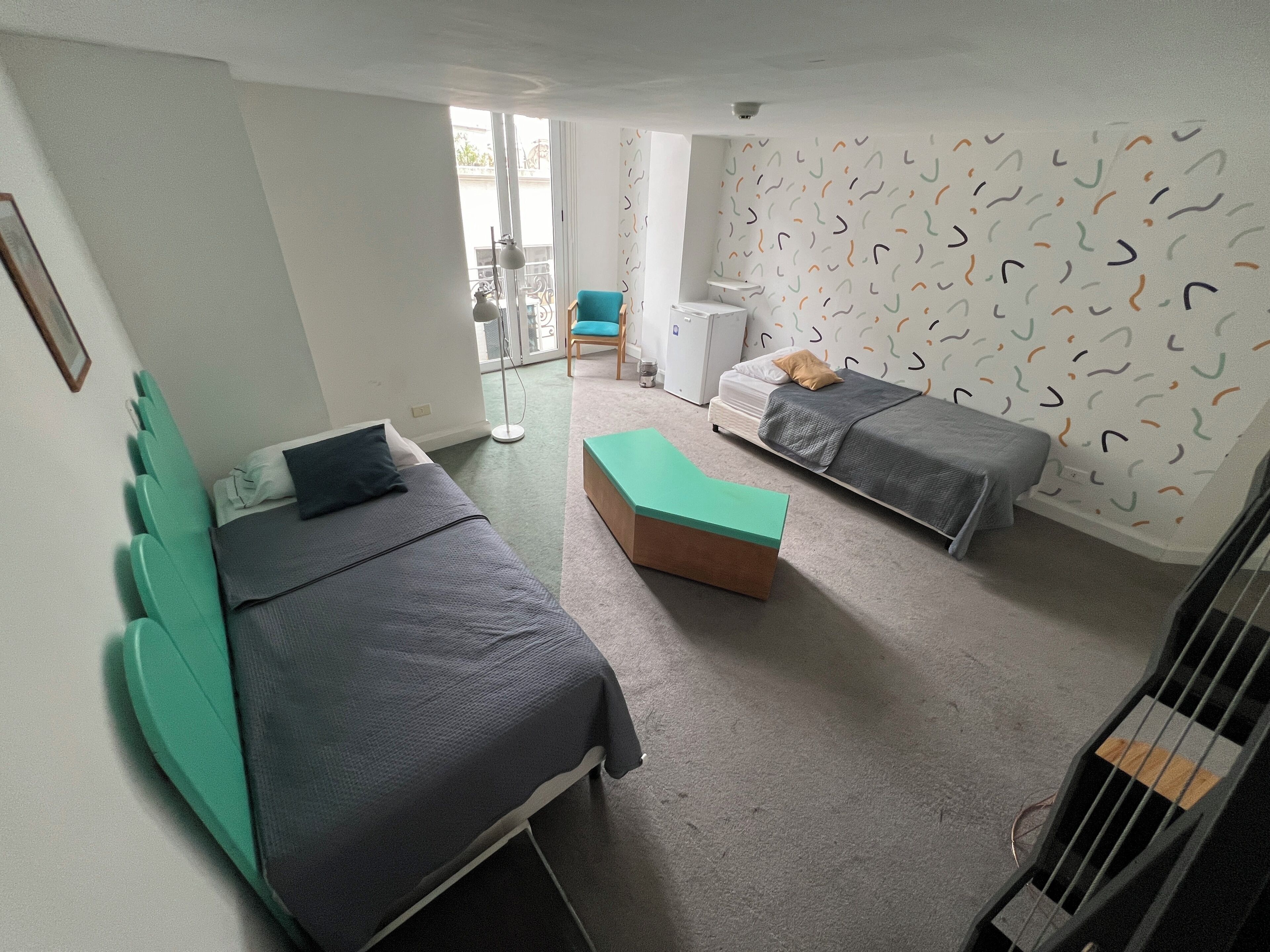 Una habitación con dos camas, una mesita y un balcón con una silla.