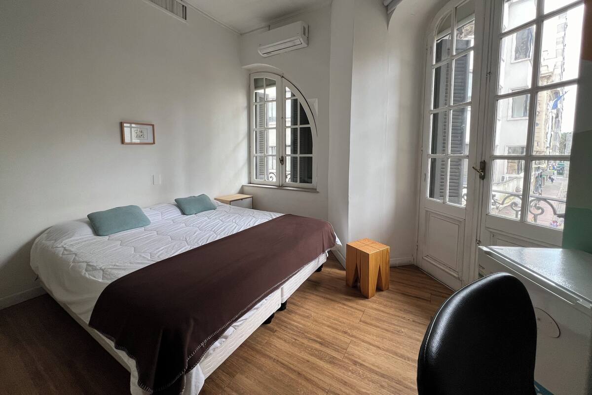 A bedroom with a large bed, a wooden stool, and a chair.