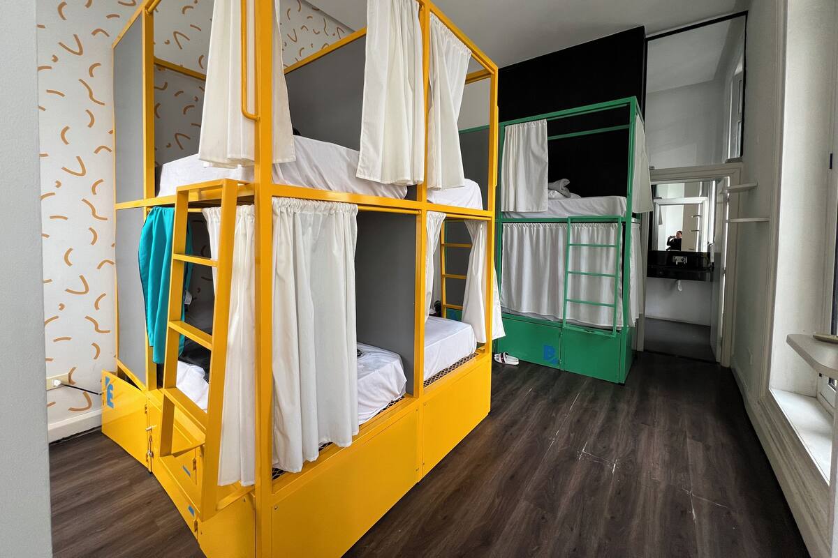 A room with a yellow bunk bed, a green bunk bed, a white sink, and a mirror.
