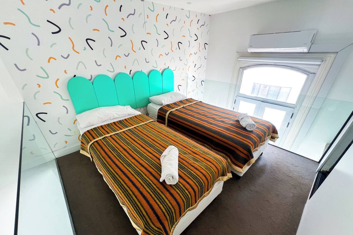 A hotel room with two beds, a teal headboard, striped bedding, and a patterned wall.
