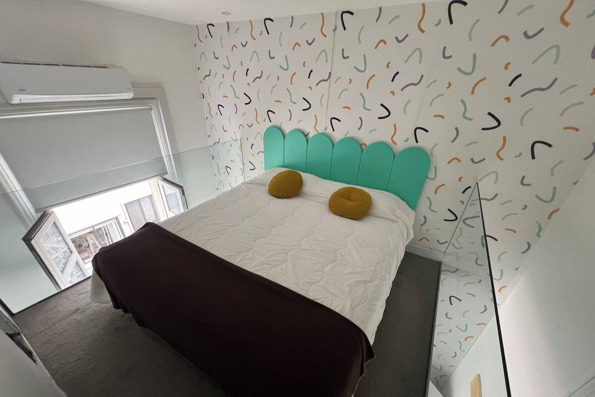 A modern hotel room with a bed, a bench, a wardrobe, and a patterned wall.