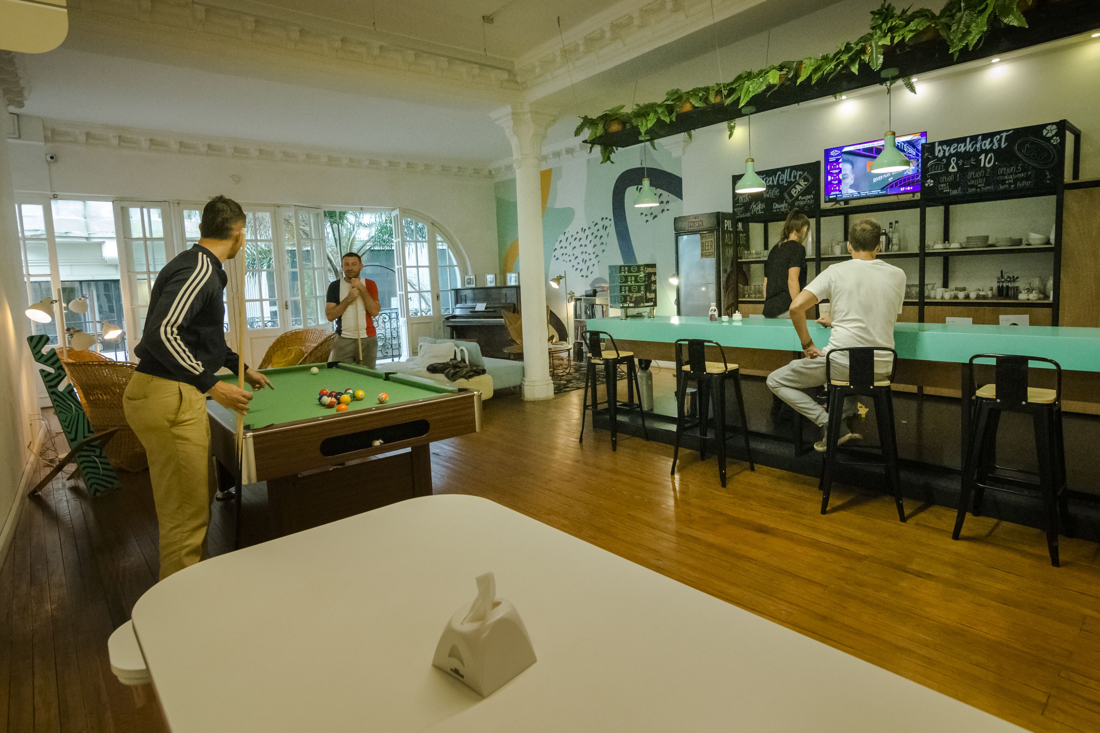 Una mesa de billar, una mesa de pool y una zona de bar con taburetes y un menú en una pizarra.