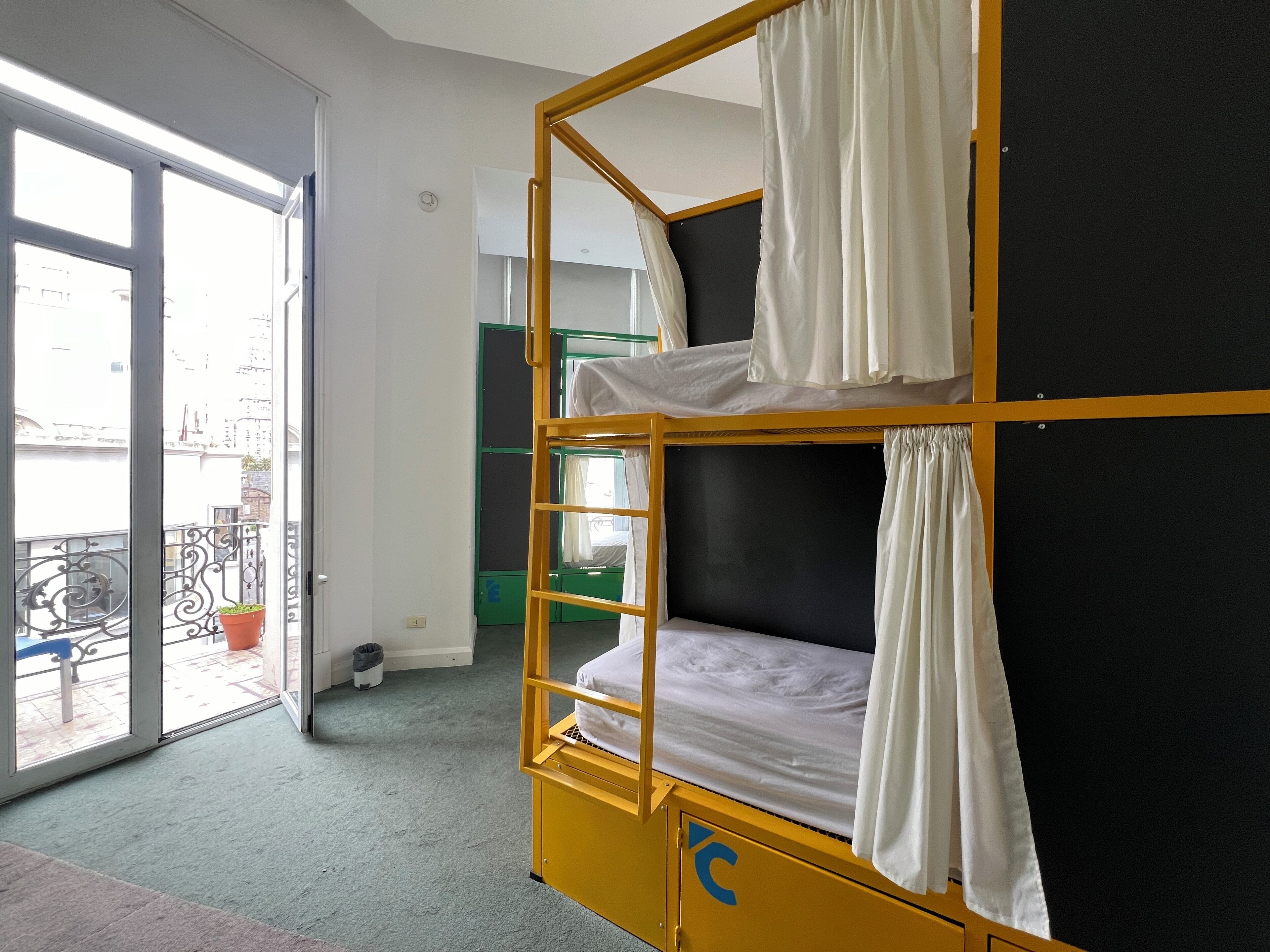 Ein Schlafsaalzimmer mit Etagenbetten, einem Balkon mit Geländer und einer Tür zu einem Außenbereich.