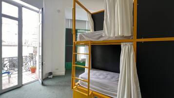 Ein Schlafsaalzimmer mit Etagenbetten, einem Balkon mit Geländer und einer Tür zu einem Außenbereich.