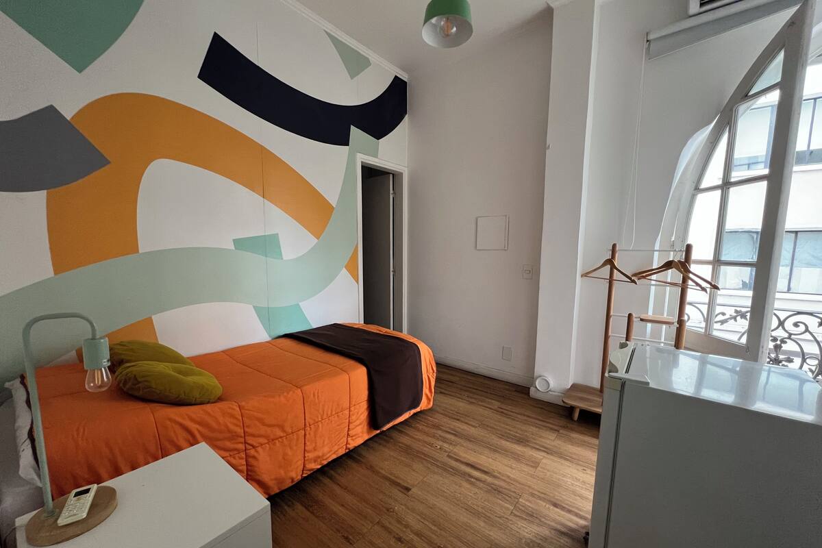 A modern bedroom with a bed, a desk, and a large window.