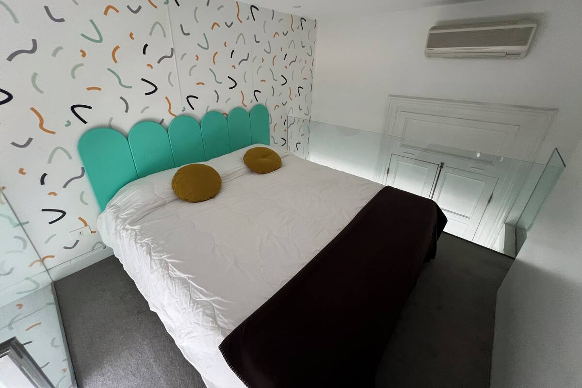 A modern bedroom with a teal headboard, white walls, and a glass cabinet.