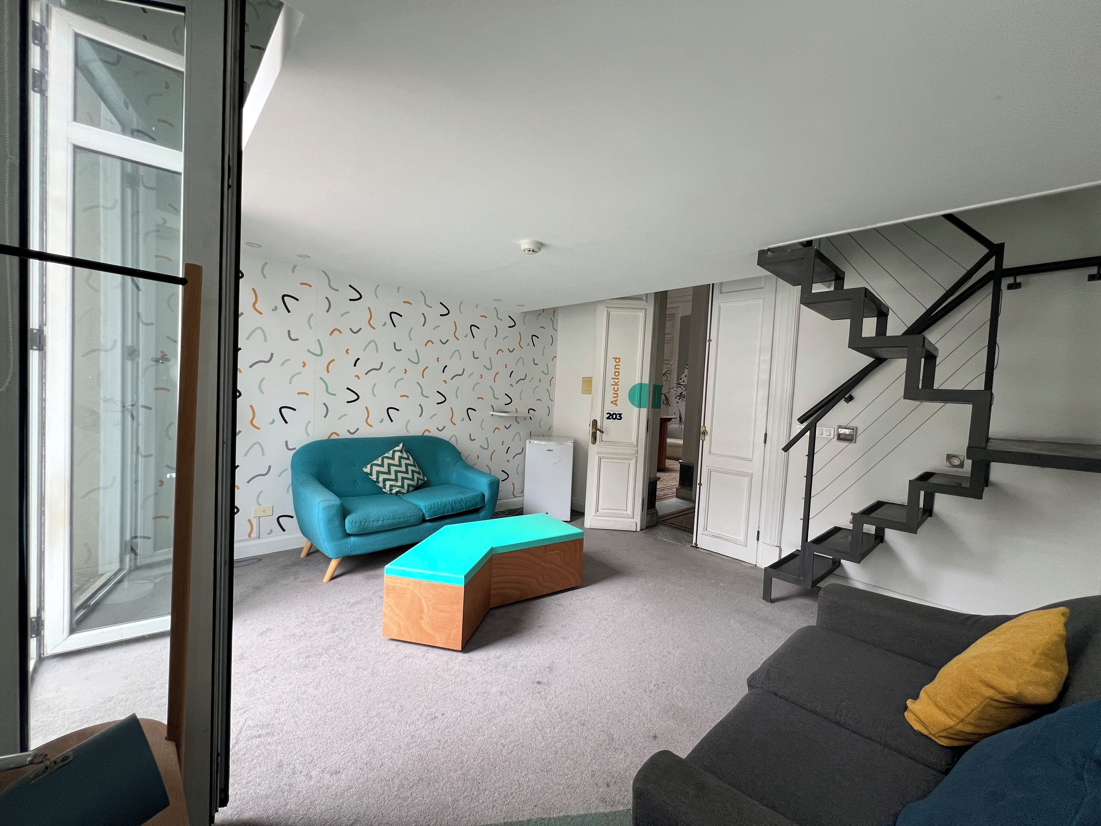 A modern living room with a sofa, a blue armchair, a wooden coffee table, and a staircase.