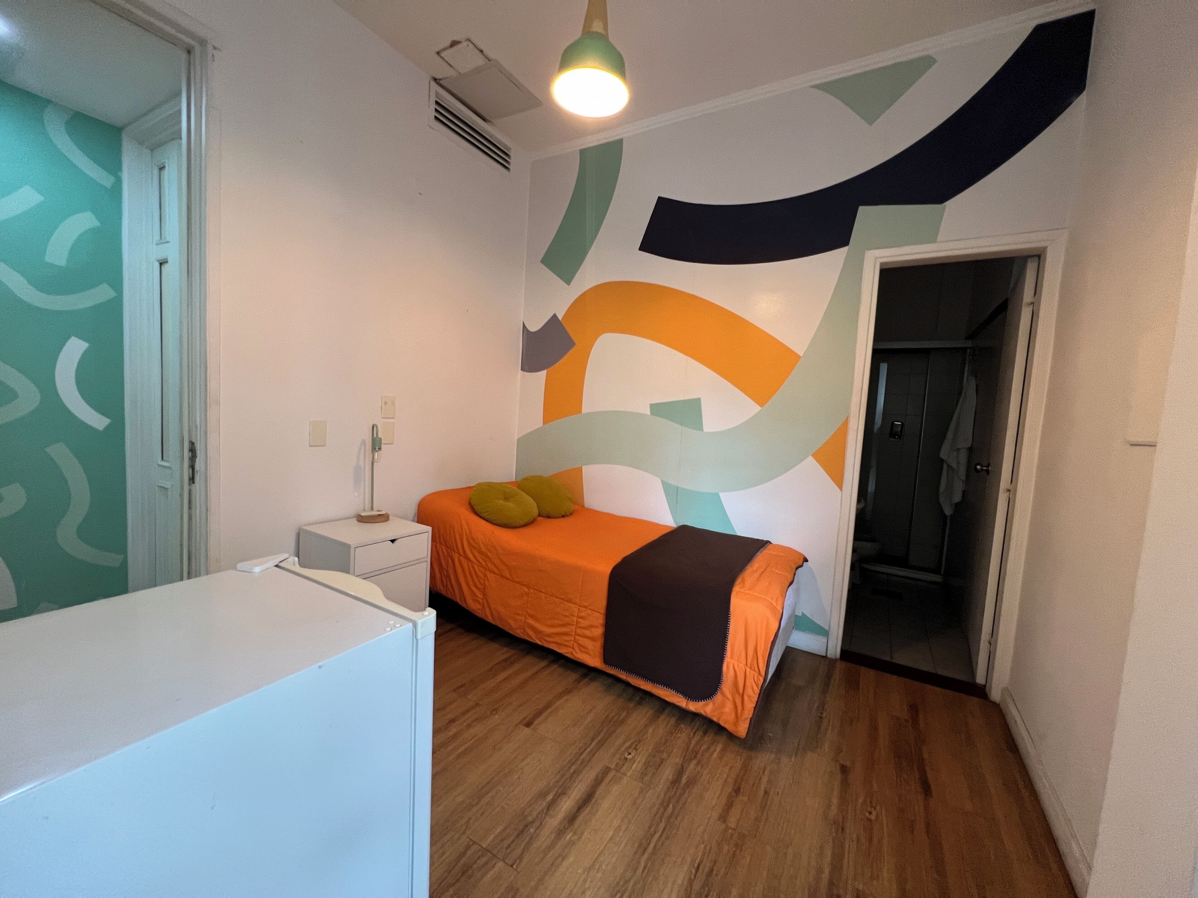 Une chambre à coucher avec un lit, une table de chevet, une lampe et un mur orné d’œuvres d’art abstraites.