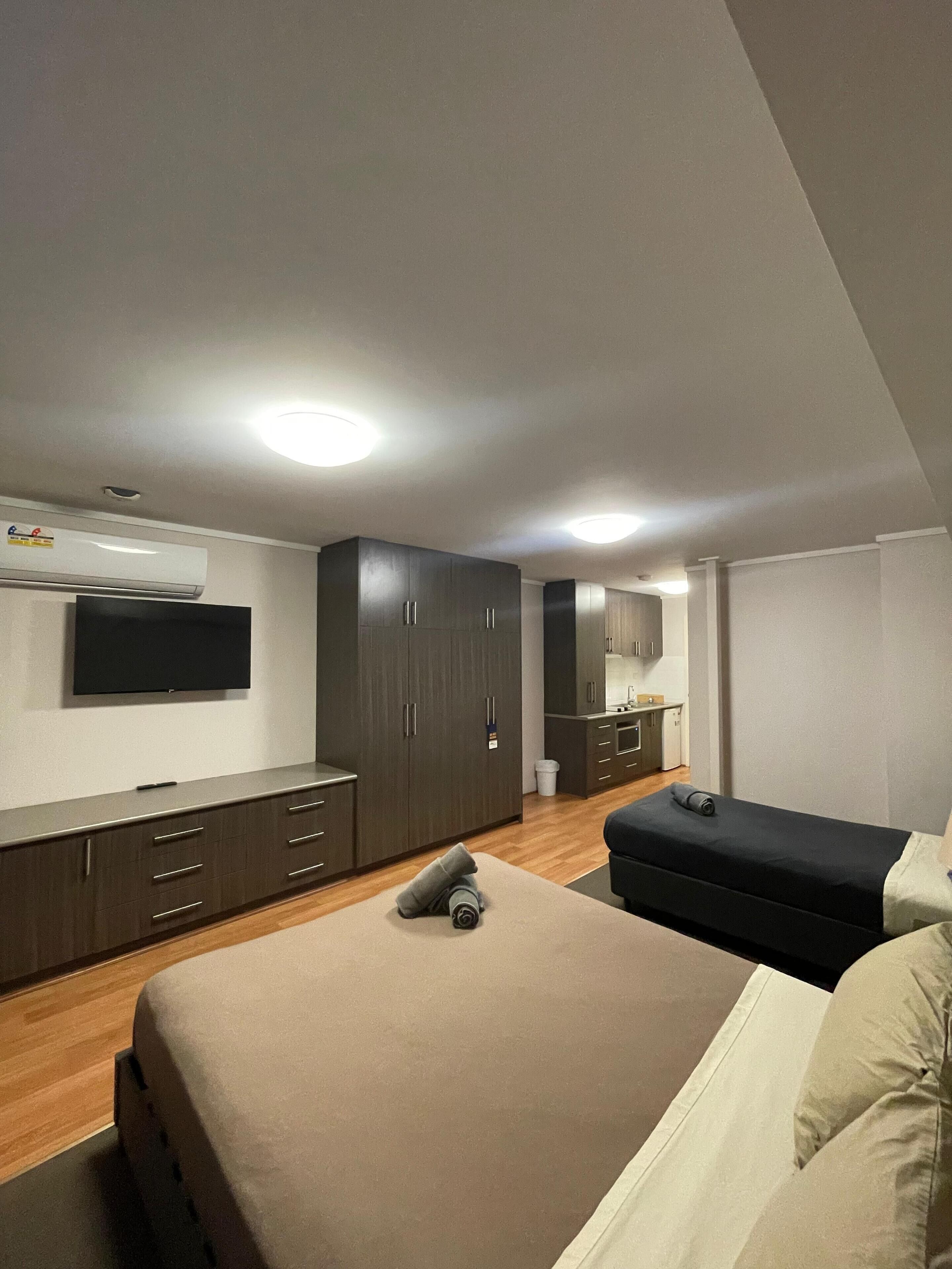 A modern hotel room with a large bed, a TV mounted on the wall, and a wardrobe.