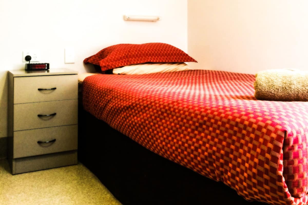 Quarto com cama, mesa de cabeceira, maleiro e ar condicionado na parede.