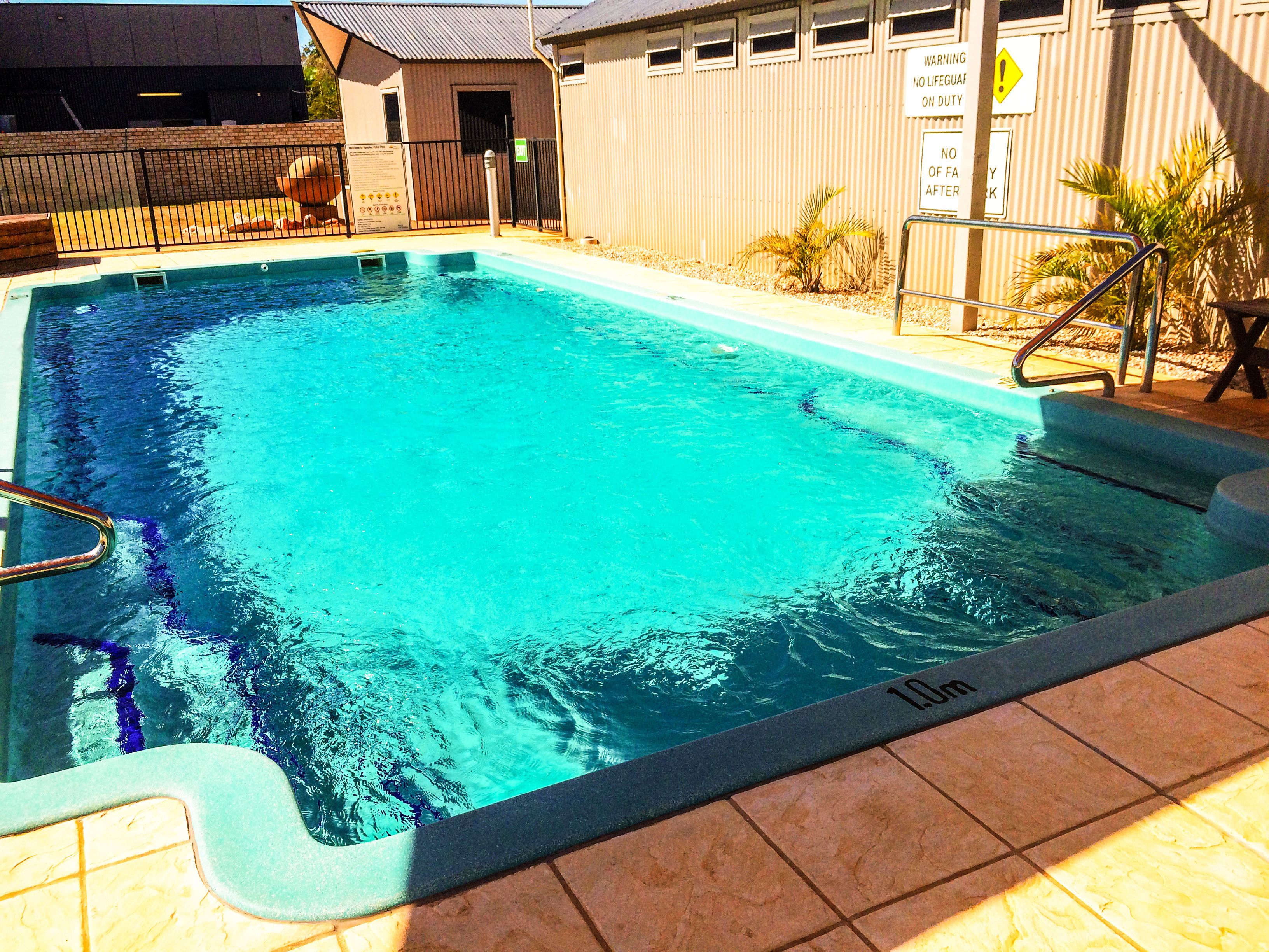 Una piscina rectangular con una escalera metálica en un lado, rodeada por una solana con azulejos.