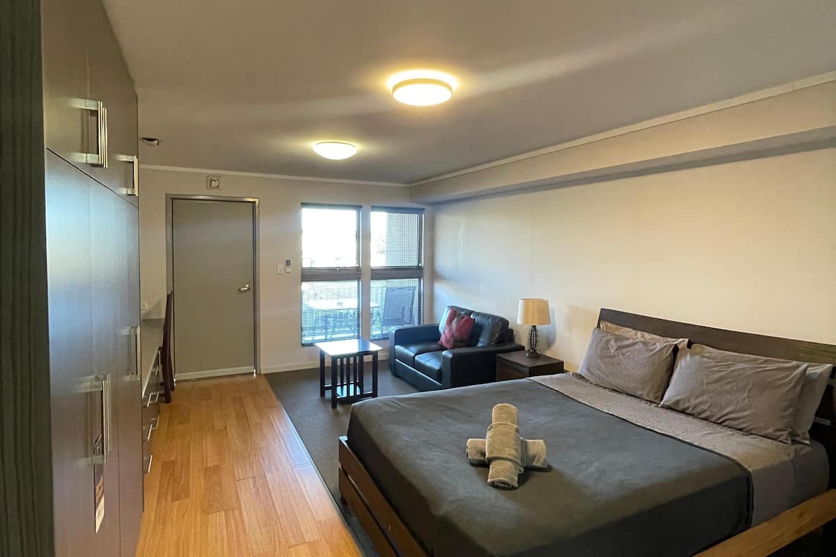 Quarto de hotel moderno com uma cama grande, uma escrivaninha pequena, um sofá e uma janela com vista.