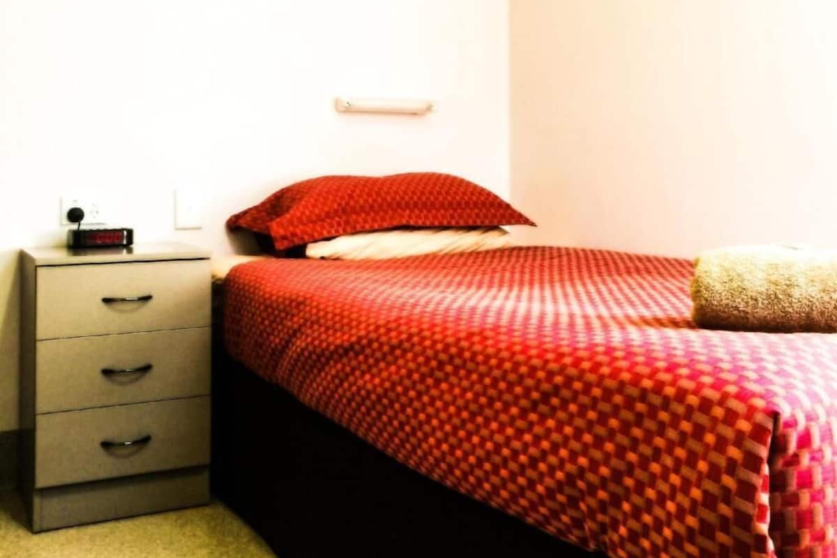 Quarto com cama, mesa de cabeceira e luminária na parede.